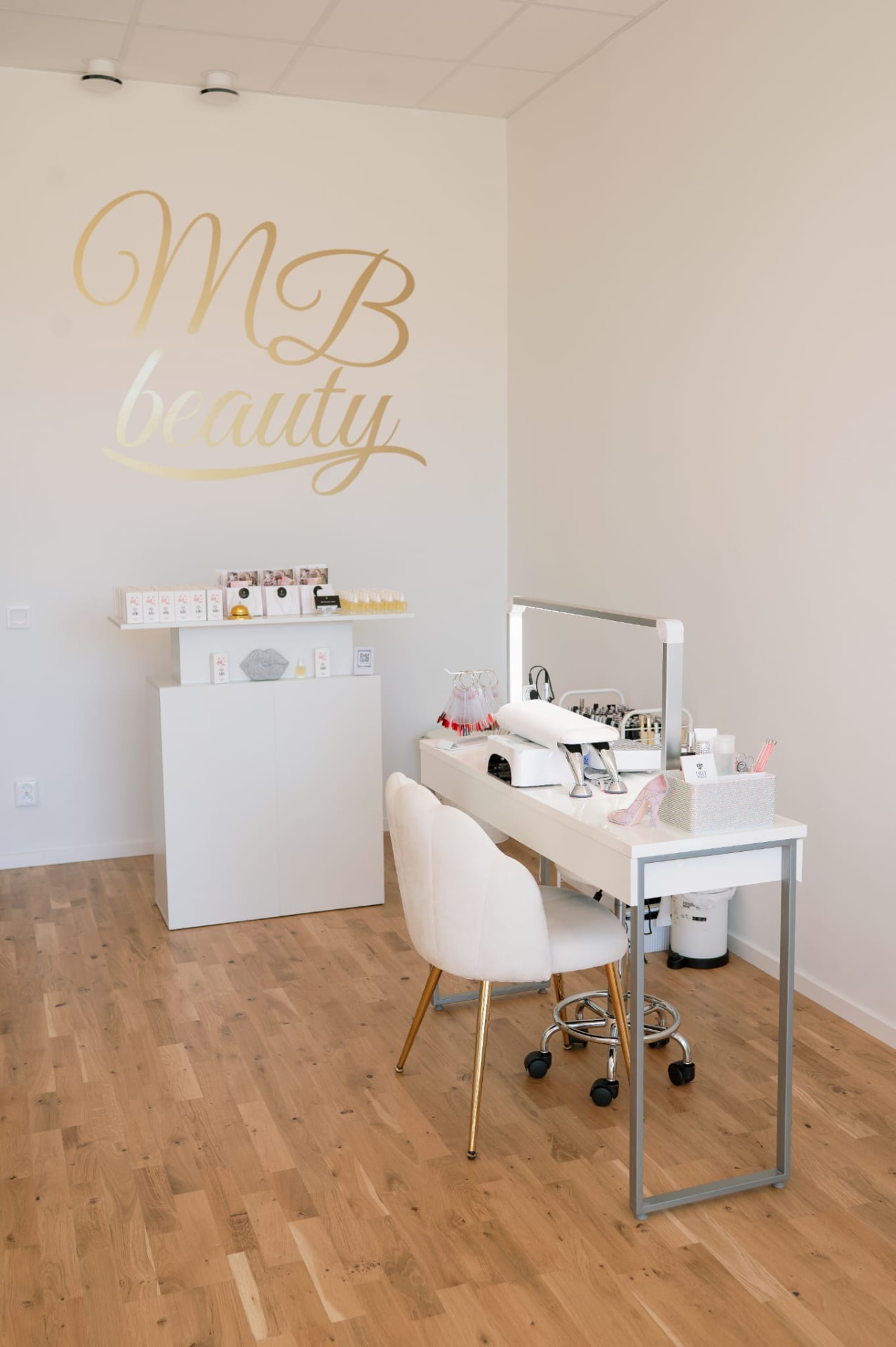 Salongen hos MB Beauty Love med MB beauty-logotyp i guld på väggen och nagelbord i vitt och ljust trä