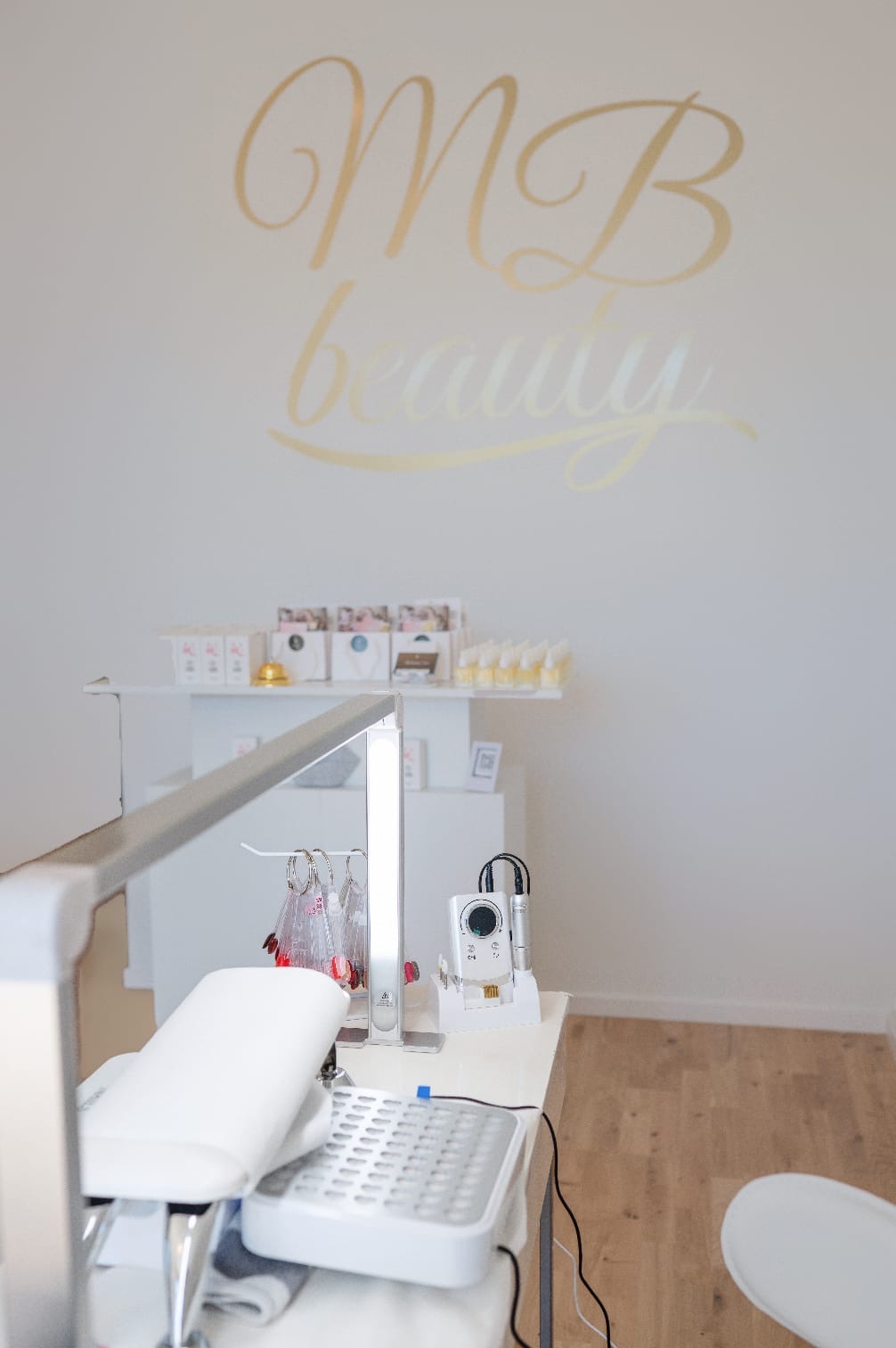 MB beauty-logotypen i guld på väggen ovanför nagelplatsen i salongen